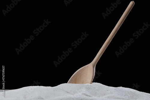 Wooden spoon scooping or mixing natural granulated sugar during cooking and baking with black background
