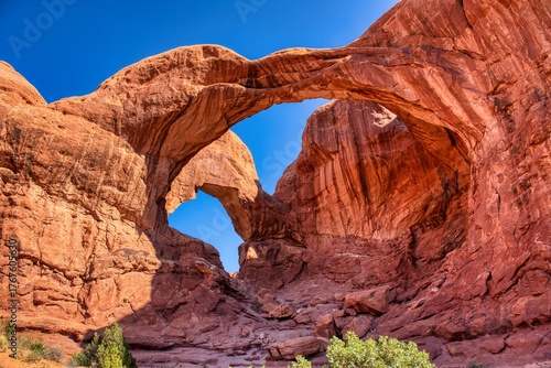 Arches Nationalpark, Moab in Utah US.. sunlit red rock desert landscape reveals towering sandstone spires and eroded fins under clear azure sky.