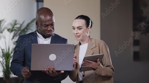 Businessman and businesswoman in a modern office discussing ideas while working on a laptop, demonstrating teamwork and professionalism.