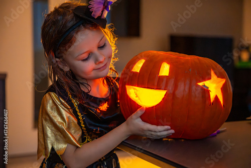 Little girl carving a Halloween pumpkin at home in the evening. Concept of childhood creativity, family tradition, and festive autumn mood.