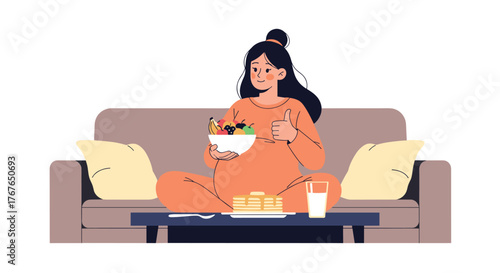 Pregnant woman sitting on a couch eating a bowl of fruit and giving a thumbs up.