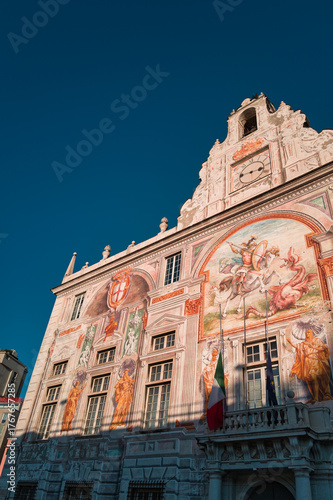 Palazzo San Giorgio in the city of Genoa under a blue sky and flags at half-mast