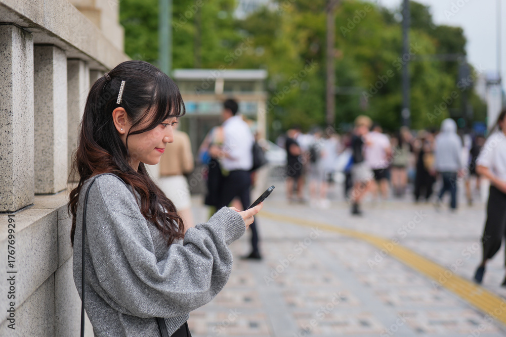 Obraz premium Young woman looking at smartphone on a sidewalk