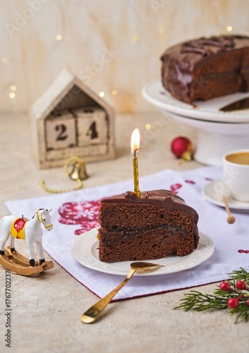 Sliced ​​homemade Sachertorte made of two chocolate layers, layered with apricot jam and covered with chocolate icing on a white plate in a Christmas theme.
