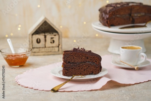 A sliced ​​homemade Sachertorte, made of two chocolate layers sandwiched with apricot jam and topped with chocolate icing, on a white plate.
