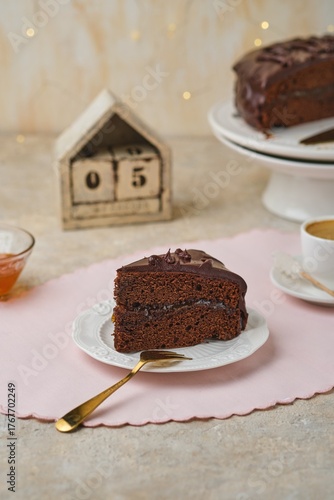 A sliced ​​homemade Sachertorte, made of two chocolate layers sandwiched with apricot jam and topped with chocolate icing, on a white plate.