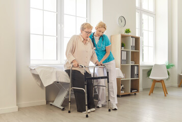 Nurse helping senior patient safe walking, elderly patient using walker to stand with support of caregiver. Mobility training and physical recovery after injury in clinic with medical staff
