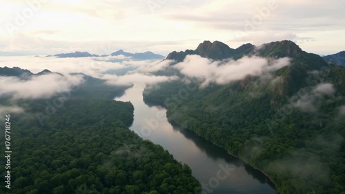 Misty Morning Over Dense Rainforest River Valley And Jagged Peaks With Soft Sunlight Breaking Through Clouds