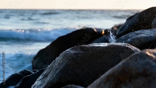 Ocean Waves Crashing On Dark Jagged Rocks At Sunset With Sparkling Water Droplets In Golden Hour Light