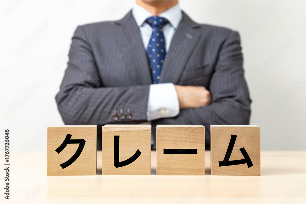 Obraz premium 「クレーム」と書かれたブロックと腕組みをするビジネスマン