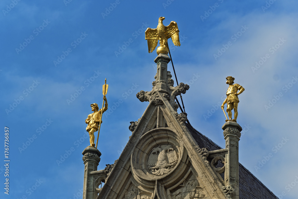Obraz premium a golden eagle with wings partially spread. Flanking the pediment are two golden statues atop columns — one holding a staff, the other a sword in Antwerp