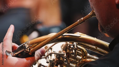 A close-up of a musician playing the French horn. The focus is on the intricate details of the instrument and the technique required to play it