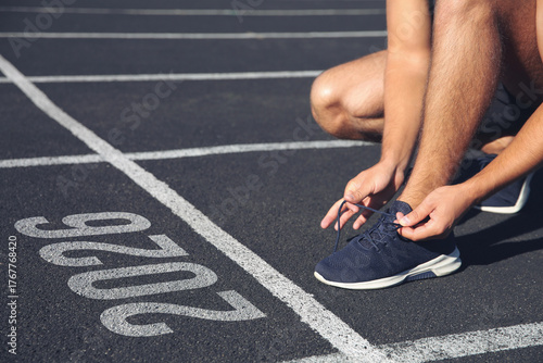 New Year. Sporty man tying shoelaces in front of line with numbers 2026 at stadium, closeup