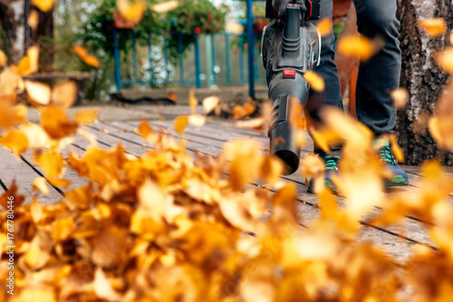 Man using handheld blower to remove dry leaves from wooden terrace during autumn yard cleaning