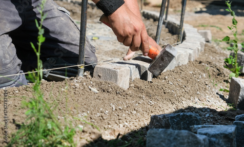 Landschaftsgärtner bei der Arbeit im Detail – präzise Handarbeit im Gartenbau mit Fokus auf Steine, Werkzeug und Struktur. Selektive Schärfe, viel Copy Space