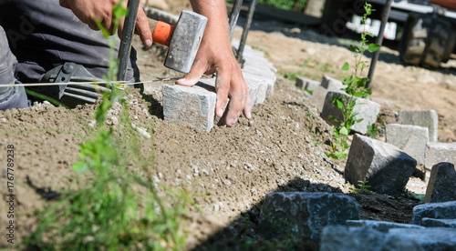 Landschaftsgärtner bei der Arbeit im Detail – präzise Handarbeit im Gartenbau mit Fokus auf Steine, Werkzeug und Struktur. Selektive Schärfe, viel Copy Space