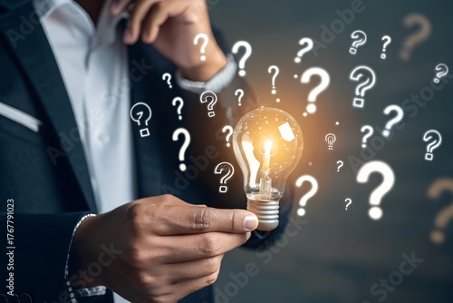 Businessman holding glowing lightbulb and question mark with copy space for creative thinking idea and problem solving concept.