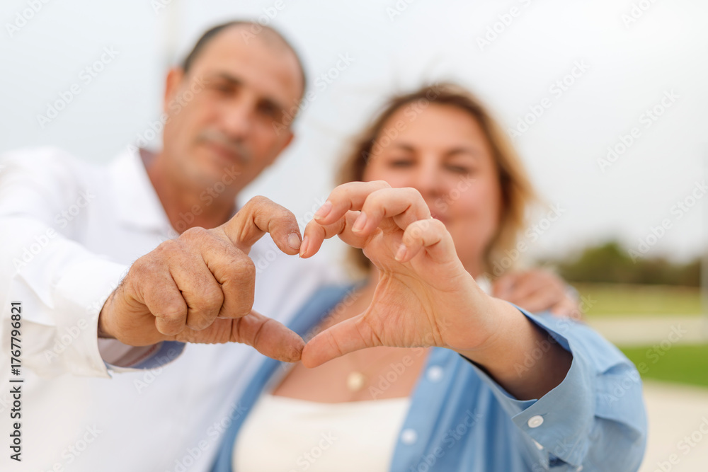 Fototapeta premium A man and woman, an older couple, make a heart with their hands.