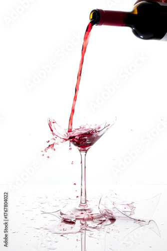 A bottle pours red wine into a broken glass. Splashes. Space available for advertising campaigns. White background.