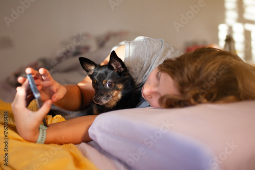 Morning moment — preteen girl with her chihuahua dog in bed using smartphone
