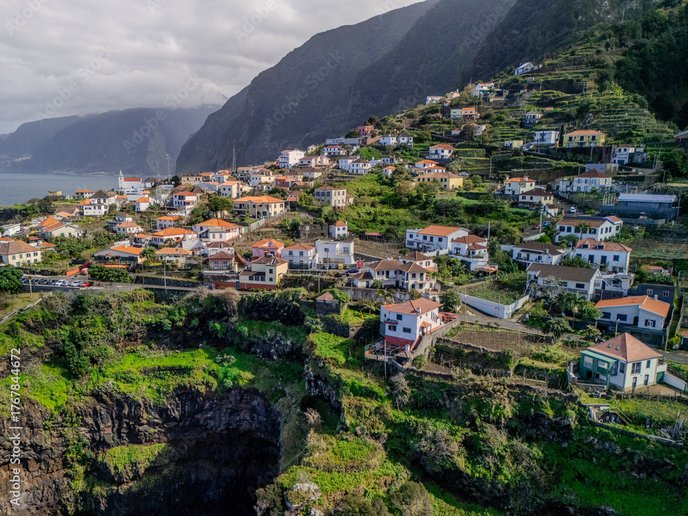 Fototapeta premium Aerial view of Seixal village on Madeira Island, nestled between steep green mountains and the rugged Atlantic coastline. 