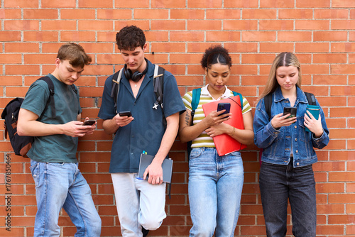 Photos Students distracted by smartphones leaning against brick wall