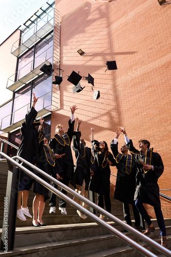Tablou pe pânză Happy students celebrating graduation by tossing caps