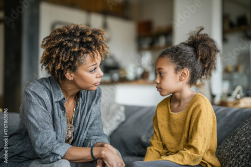 Woman and girl sitting on couch at home and having a serious conversation