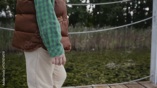 Side view close-up of boy walking by the lake on wooden pier. Emphasizes healthy outdoor lifestyle and calm presence. High quality 4k footage