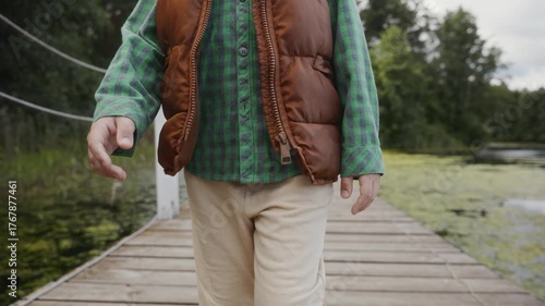 Medium close-up of boy in vest and shirt walking on pier. Symbolizes healthy lifestyle, balance and natural connection. High quality 4k footage