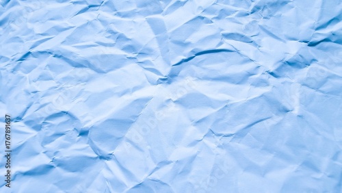 Full frame, high-angle view of wrinkled, crumpled light blue paper texture, creating an abstract and distressed background or backdrop.