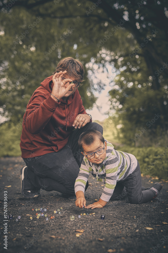 Fototapeta premium Adult man and his son training classic marbles outdoor on pathway in nature