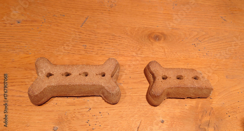 one large dog bone biscuit next to half a broken dog bone biscuit on an oak tabletop
