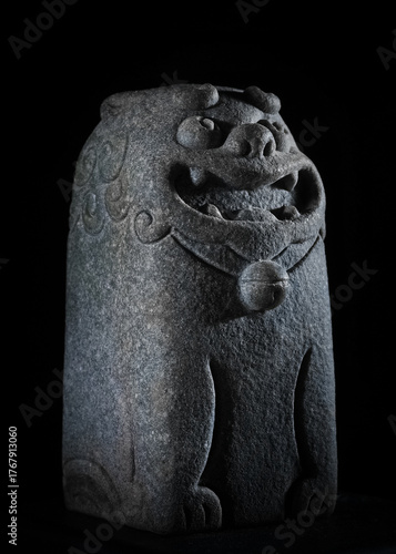 Ancient stone lion statue with intricate carvings on a black background.