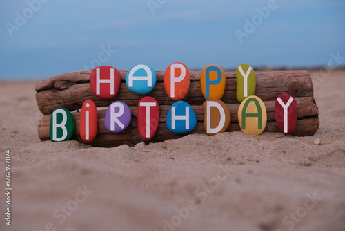 Creative Happy Birthday message composed with hand painted multi colored stone letters on the beach