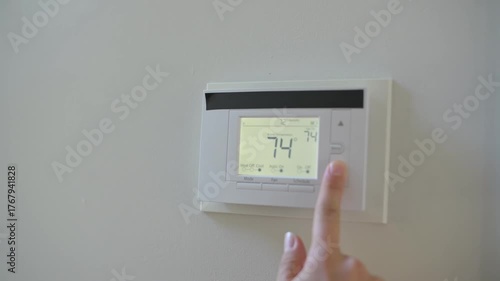 A person presses a button on a digital wall thermostat to change temperature. Adjusting wall thermostat thermostat