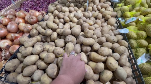 Close-up of Hand Selecting Fresh Potatoes at Supermarket Produce Section: Healthy Eating Grocery Shopping.