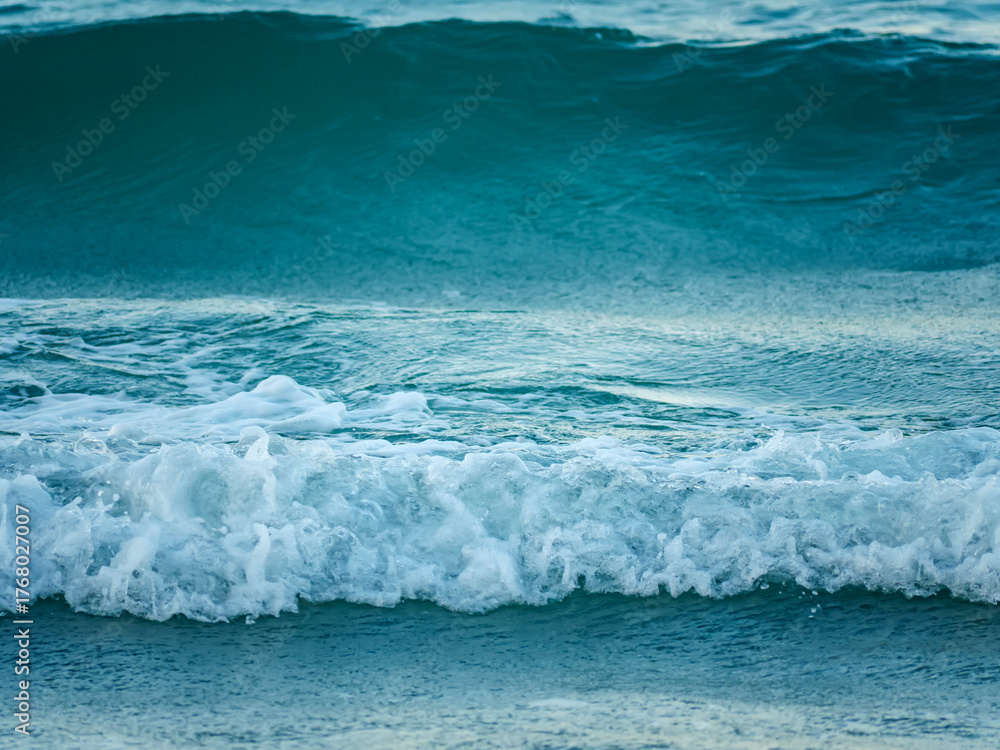Obraz premium A beautiful and dynamic close up of a turquoise sea wave breaking into white foam as it moves across the water surface on a sunny day