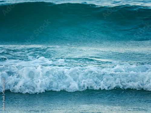 Fototapeta Naklejka Na Ścianę i Meble -  A beautiful and dynamic close up of a turquoise sea wave breaking into white foam as it moves across the water surface on a sunny day