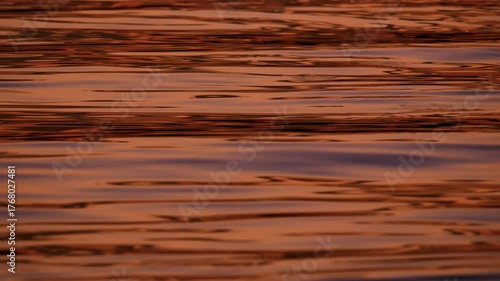 A beautiful and warm abstract background video of a calm sea surface with intense golden and orange sunset reflections