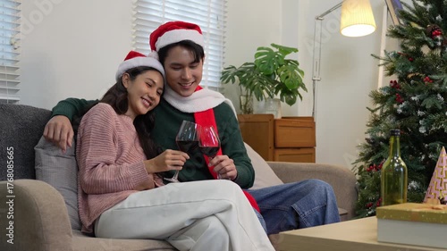 Happy Asian couple celebrating Christmas sharing warmth in winter embrace, exchanging gifts on sofa in cozy home.