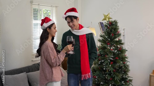 Happy Asian couple celebrating Christmas sharing warmth in winter embrace, exchanging gifts on sofa in cozy home.