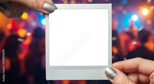Hands holding blank instant photo frame at a lively party with blurred lights and dancing people, creating a fun and festive atmosphere.