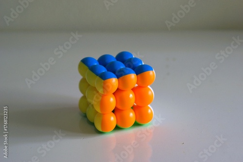 colorful 3D puzzle cube made of round plastic pieces in blue, orange, and yellow colors placed on a clean white surface