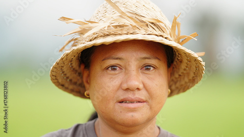 closeup portrait of an indonesian woman rice farmer in a straw hat in rural indonesia, women in agriculture, serious face, looking at camera, headshot