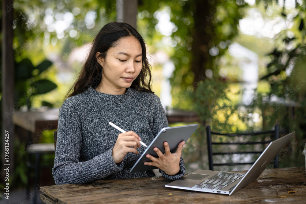 Obraz premium Asian freelancer designer using tablet with stylus at outdoor cafe