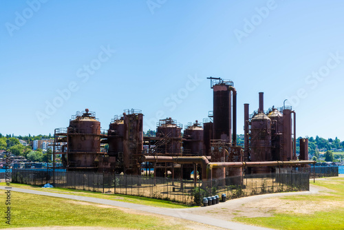 Side view of the a former oil plant fenced in and surrounded by a wide lawn under a clear blue sky. Taken while walking in the Seattle urban area on a clear July day, specifically in Gas Works Park.
