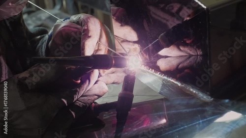 An industrious and technical mood is captured by a close-up of a welder in protective gear using a welding torch, with the bright arc and reflection visible in the shield and surrounding surfaces