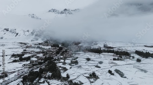 Aerial drone shot of traditional Ladakhi village houses and structures partially covered in snow in the Himalayan mountains.