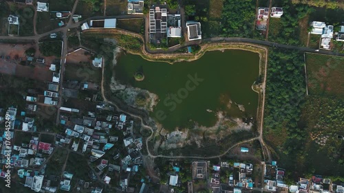 aerial drone shot of a small lake or pond in a rural Indian village, surrounded by fields and homes.